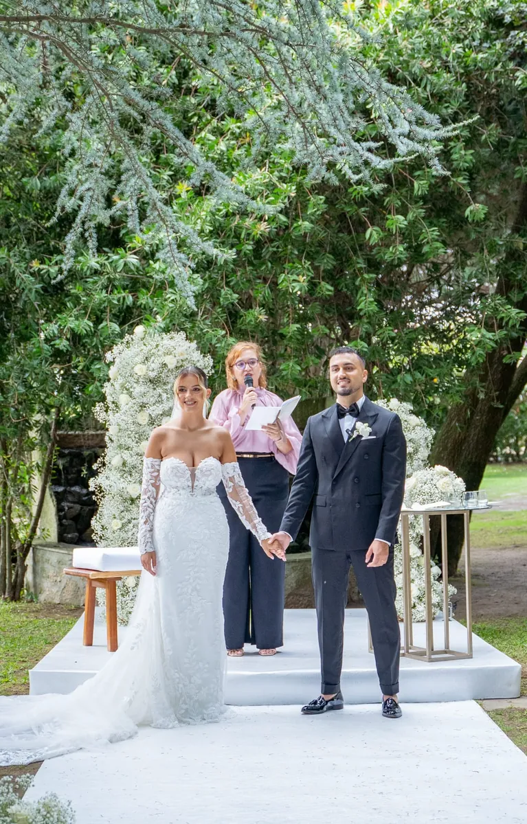Os noivos de mãos dadas junto ao arco floral